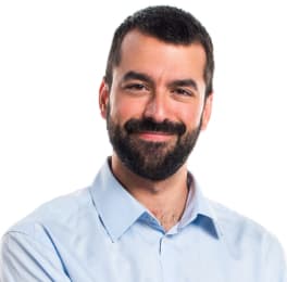 Mark Guerrero wearing a light blue collared shirt, standing with arms relaxed in a professional studio setting with a white background, neutral and confident expression